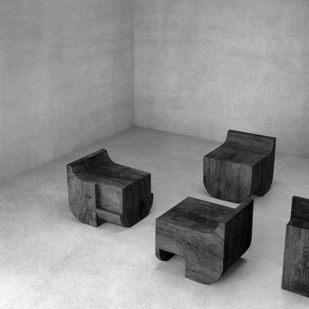 Ebonized monolithic wood chairs carved from solid timber by sculptor Isac Elam Kaid in a minimalist architectural interior.