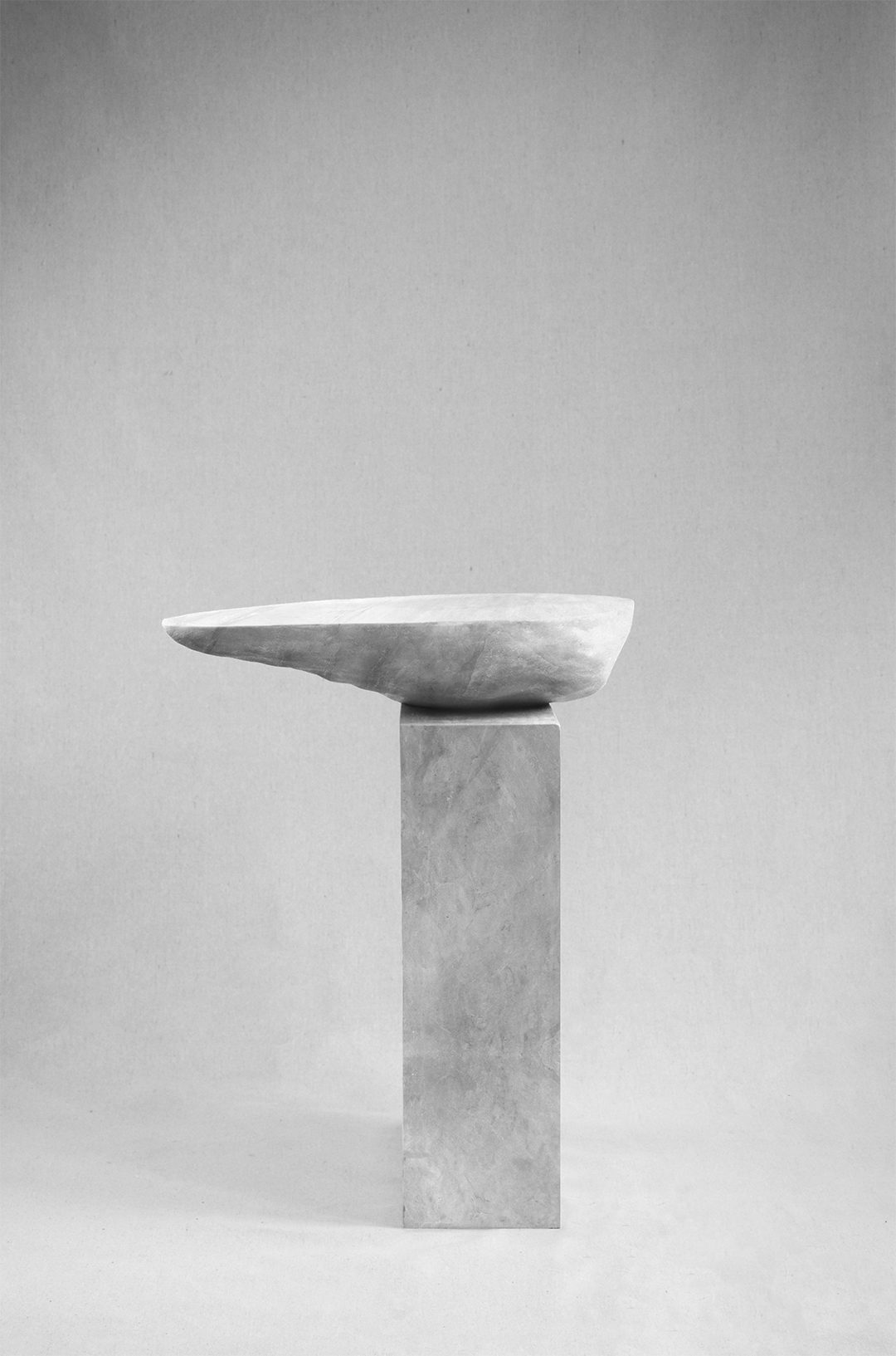 Asymmetrical stone side table by Isac Elam Kaid with an irregular eroded stone top balanced on a rectilinear stone plinth.